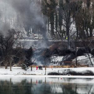 An exploded train along the riverside in Mt. Carbon, West Virginia. There is snow on the ground and smoke emitting from the burned train.