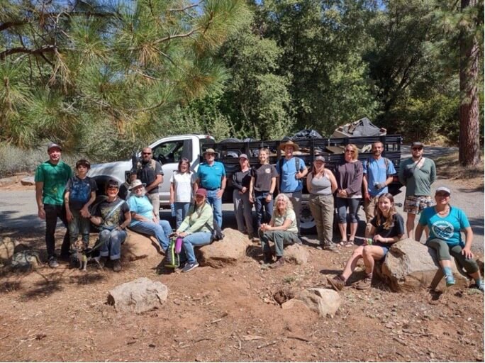 Volunteers in outdoor gear stand in front of a pickup truck with trees in the background, as they get ready to do a river cleanup along the Tuolumne River.