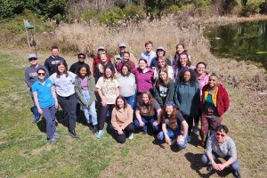 Climate Corps cohort members gather outside for a group photo. Everyone is smiling, standing on the grass by the water.