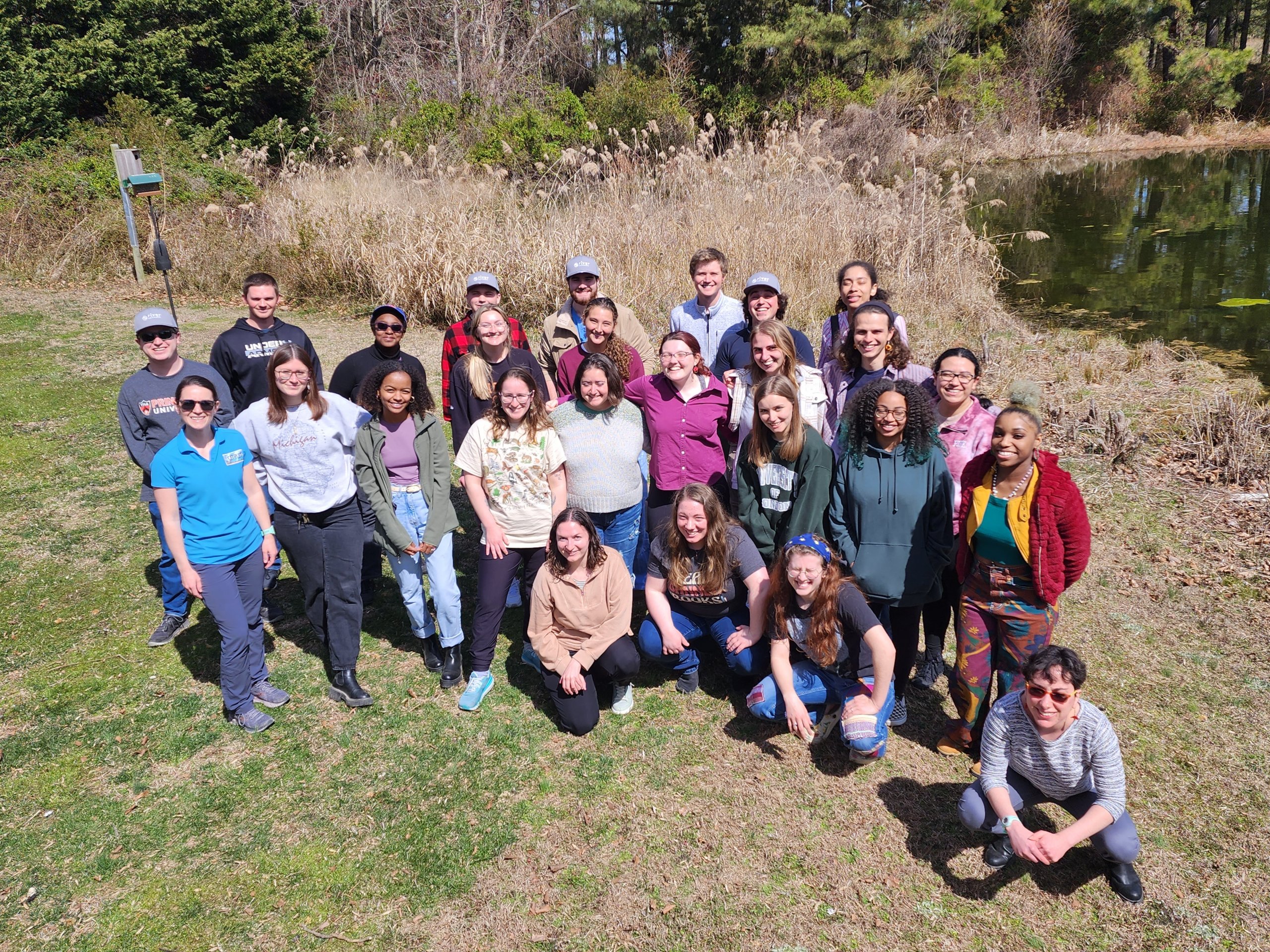 Climate Corps cohort members gather outside for a group photo. Everyone is smiling, standing on the grass by the water.