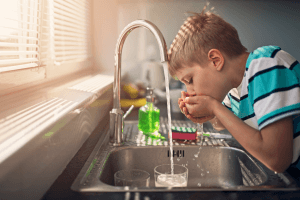 young boy drinking water from a tap