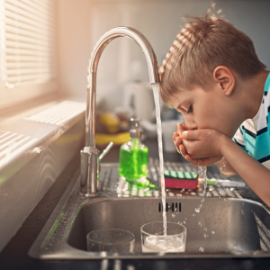 young boy drinking water from a tap